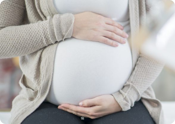 closeup on pregnant woman's stomach with her hands lovingly held above and below her belly.